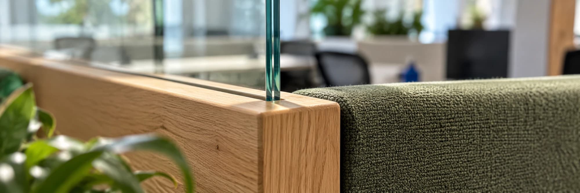 Glass, timber and green fabric meeting at the corner of a workspace partition