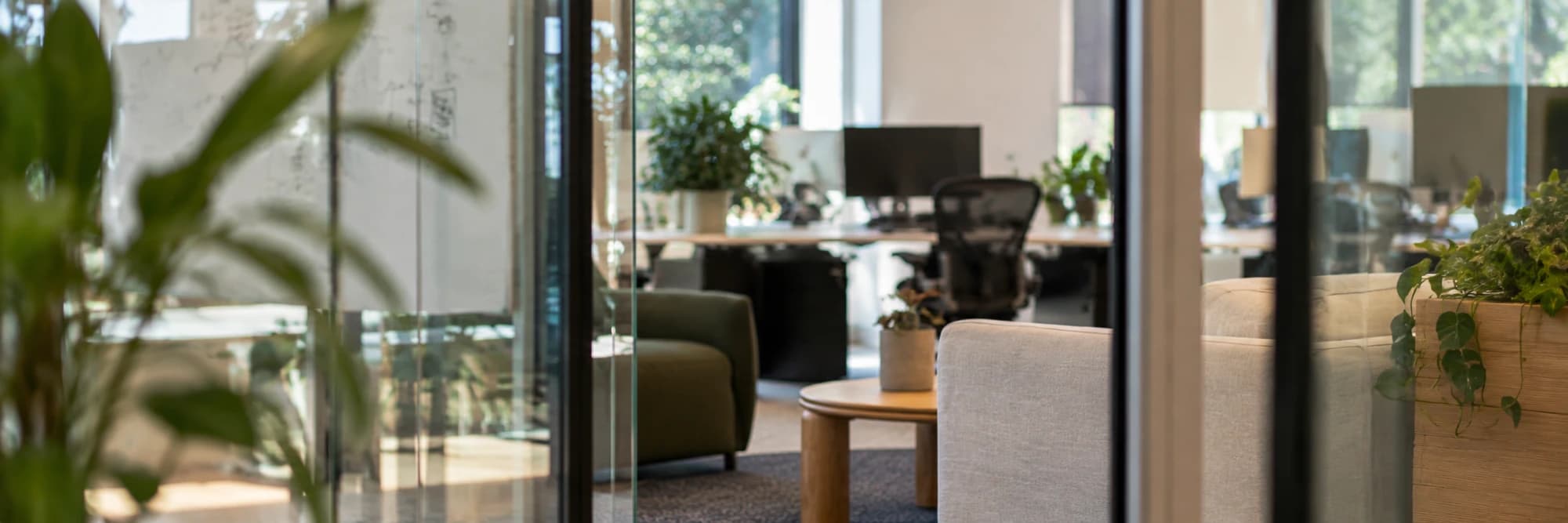 The office seen through overlapping glass partitions, the lounge and desks beyond