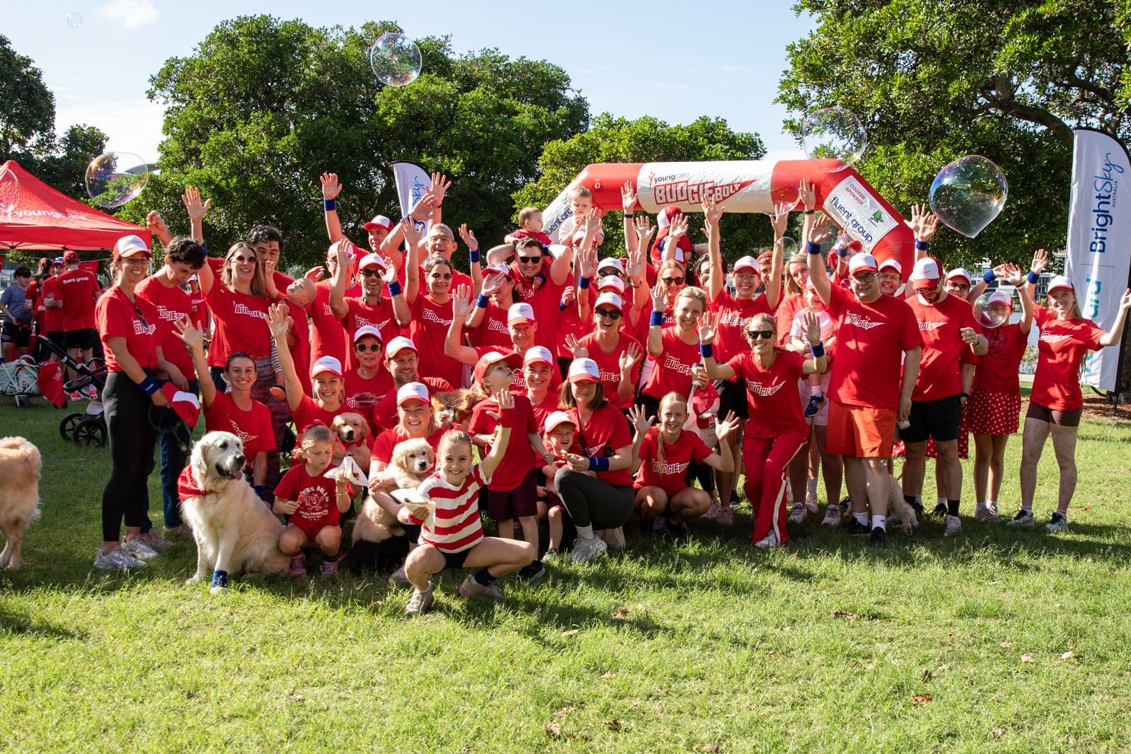 The Fluent team in the Budgie Bolt crowd, red shirts and caps, two golden retrievers at the front