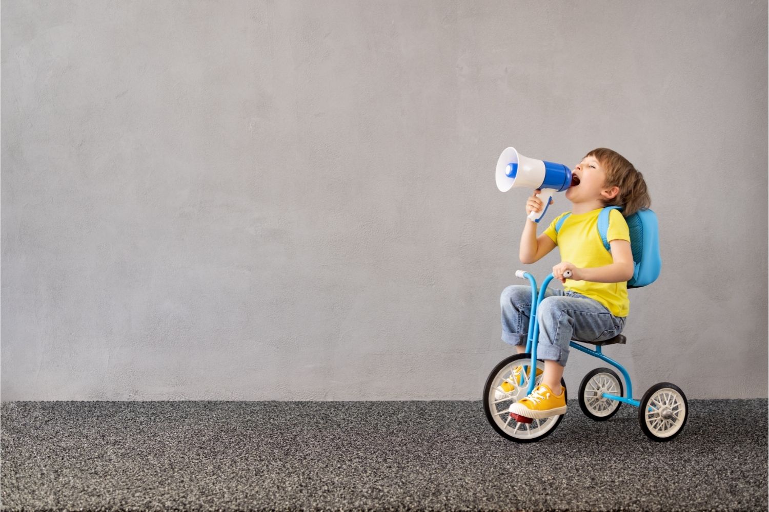 child riding a tricycle, while yelling into a plastic megaphone