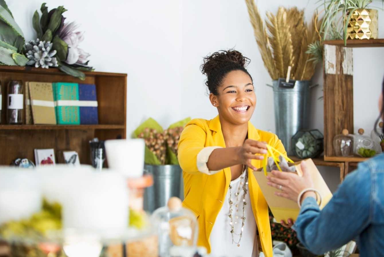 A smiling woman wearing a yellow jacket handing someone a bag